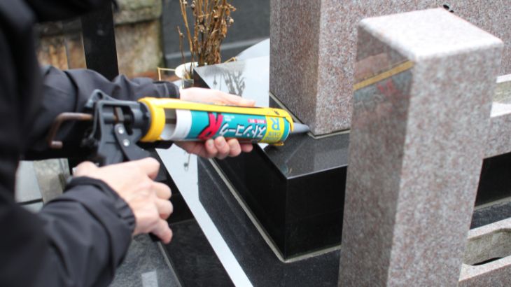 お墓の目地を補修するのに、コーキングとガンで施工をする準備をしている画像